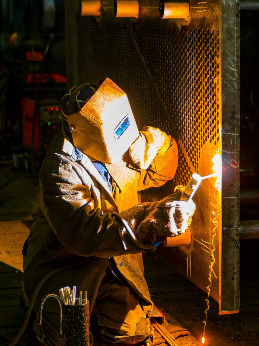 A welder in protective gear working on a steel fabrication